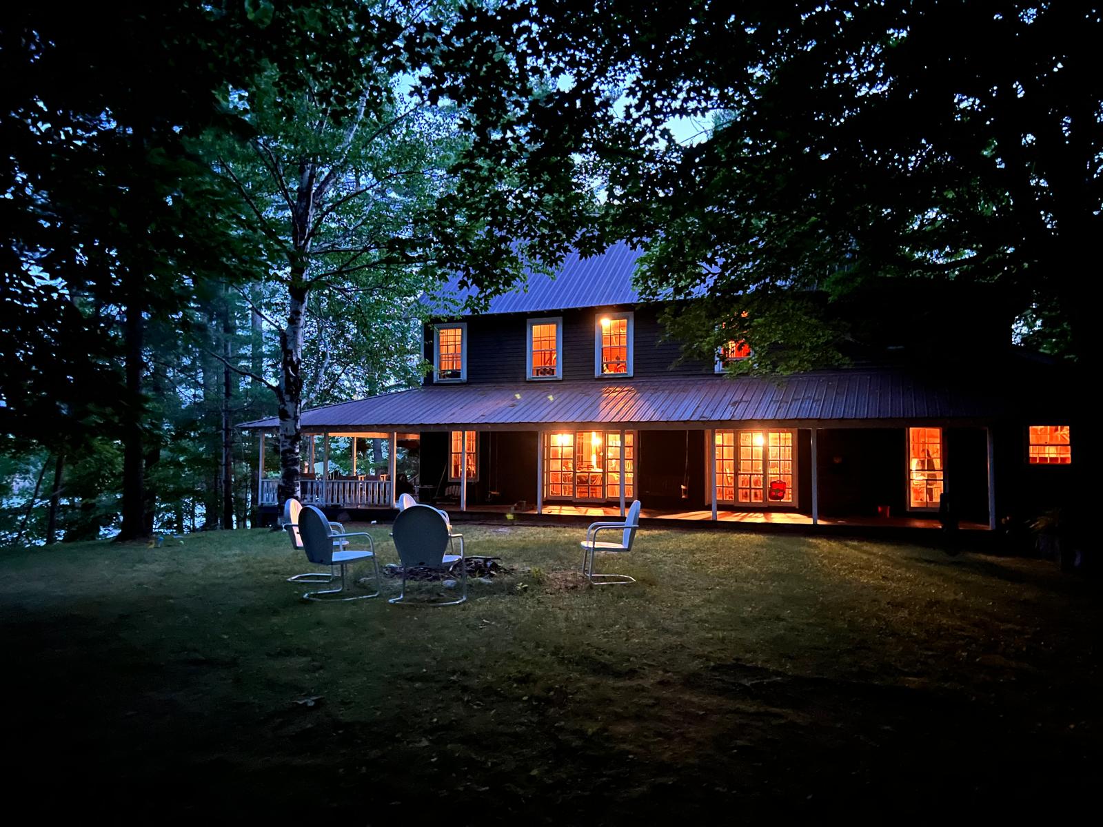 The Main House lit up at dusk, chairs around the fire pit